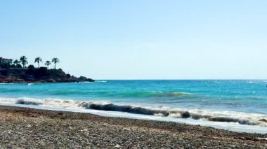 Halk plajı, yaz mevsimi, güzel güneşli hava. Resimli plaj, kumlu kıyıya vuran dalgalar. Deniz dalgaları kayalara çarpıyor. Kıbrıs adası, şemsiyeler, turist botları, Akdeniz.