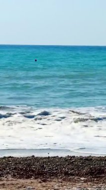 Halk plajı, yaz mevsimi, güzel güneşli hava. Resimli plaj, kumlu kıyıya vuran dalgalar. Deniz dalgaları kayalara çarpıyor. Kıbrıs adası, şemsiyeler, turist botları, Akdeniz.