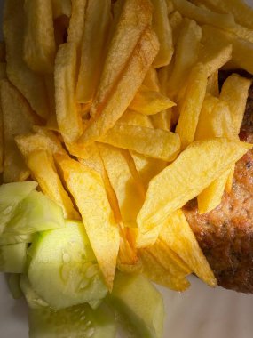 Hazır yemek: Kızarmış patates, taze salatalık, biftek. Beyaz bir tabakta hazırlanan yemeğin yakın plan çekimi..