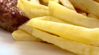Prepared food: fried potatoes, sliced fresh cucumber, pork burger patty. Close-up of the prepared portion on a white plate.