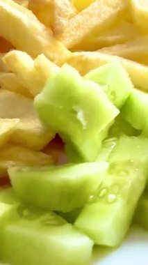 Prepared food: fried potatoes, sliced fresh cucumber, pork burger patty. Close-up of the prepared portion on a white plate.
