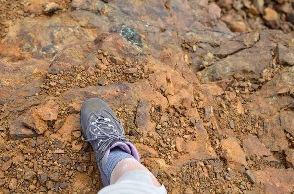 Top view of a foot in hiking shoe on a surface of orange dirt and stones