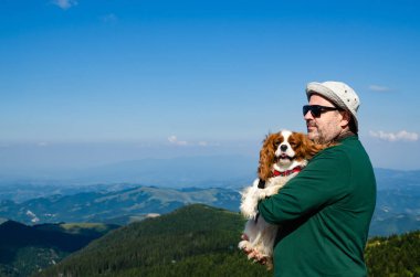 Adam köpeğini - Cavalier King Charles Spaniel - tutan bir dağ manzarası