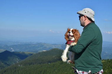 Adam köpeğini bir dağ manzarası izlerken - Cavalier King Charles Spaniel - holding