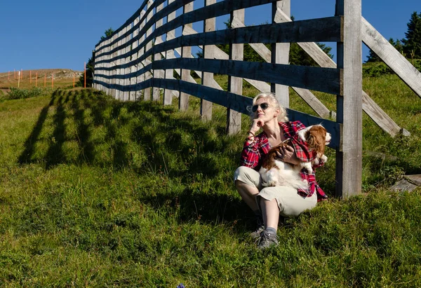 Woman dressed in rustic royal stewart shirt resting and holding her pet - Cavalier King Charles Spaniel