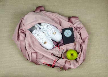 Beyaz spor ayakkabılı, yeşil elmalı ve akıllı telefonlu pembe spor çantası.