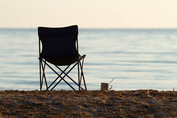 folding tourist chairand a cup on the beach in the early morning. calm.