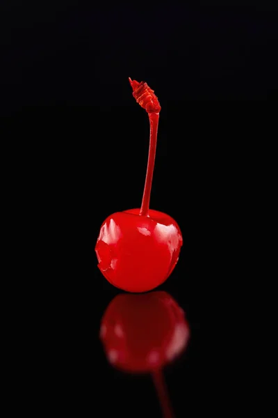 Macro image of single cocktail cherry with reflection isolated at black background.