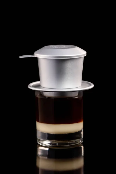 Closeup glass of vietnam coffee with aluminium filter for dripping isolated at black background.