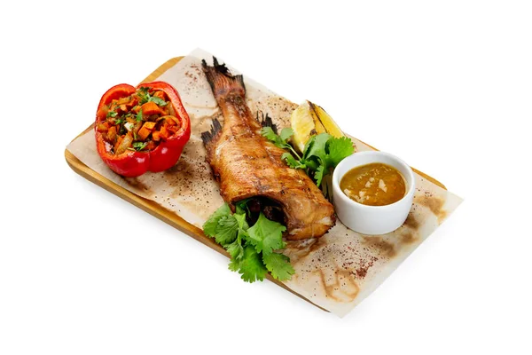 Grilled fish with no head served on paper at wooden board with p