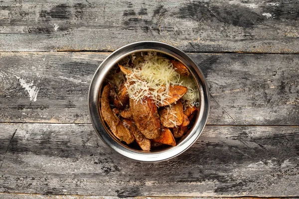 Bowl of baked potatoes slices with cheese at rustic wooden table