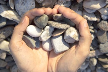 Kadın elleri sahilde taşlara dokunuyor. Gri taşlar