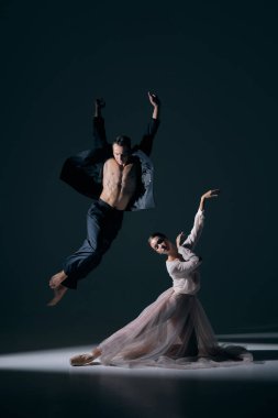 Erkek dansçı, kadın ortağın üzerinde yükseğe sıçrıyor. Sahne ışıkları altında zarifçe poz veriyor. Sahne sanatları, dramatik ifade, sahne anlatımı, modern dans ve duygusal yoğunluk kavramı.
