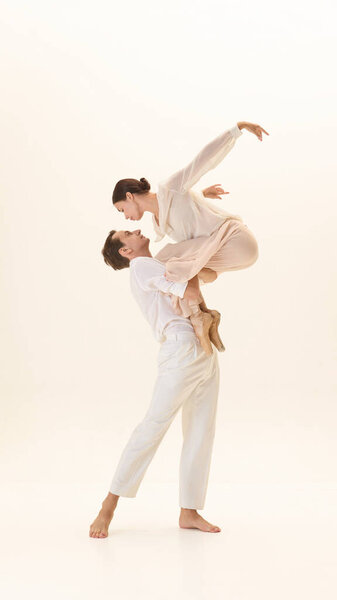 Балетная пара поднимает в белых костюмах с изящным движением, гармоничная осанка освещена в минимальной обстановке. Концепция фитнеса, элегантности, романтики, художественной связи и эмоционального доверия.
