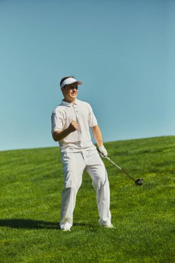 Gülümseyen golfçü yeşil sahada kaldırılmış yumruk atma kulübüyle kutlama yapıyor. Zafer kavramı, yaşam tarzı markalaşması, motivasyon, başarı ve neşeli duygularla güven..