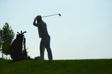 Golfçü yeşil tepe arka planında golf çantasıyla salıncak silueti hazırlıyor. Açık hava sporları, disiplin, odaklanma, eğitim, yaşam tarzı ve sağlıklı aktif eğlence kavramı.
