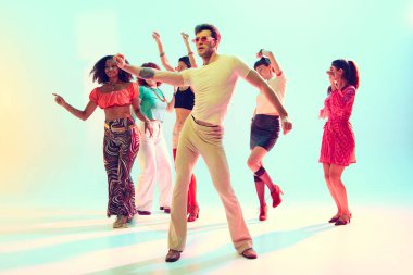 Renkli stüdyo ışığı altında dans eden bir grup şık genç. Dans etkinlikleri, gençlik partileri, moda enerjisi ve kültürel ifade kavramı.