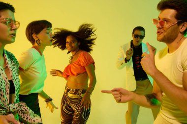 Sarı neon ışıklarının altında neşeyle dans eden farklı arkadaşlara yakın çekim. Kültürel kutlama kavramı, gece hayatı ifadesi, eski moda, müzik havası ve mutlu yaşam tarzı..