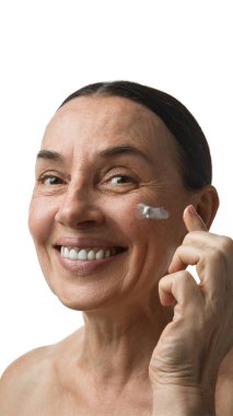 Krem sürerken gülümseyen olgun bir kadın. Yaşlanma karşıtı, cilt bakımı, cilt bakımı, güzellik rutini ve neşe dolu sağlık duygusu kavramı..