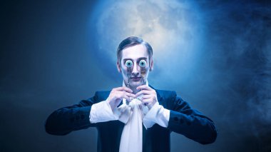 Gerçek dışı damat dolunayda göz teatral bir ifade takınıyor. Cadılar Bayramı kavramı, korku hicvi, yenilikçi başyazı, müzik kapağı tasarımı ve gerçeküstü hikaye anlatımı..