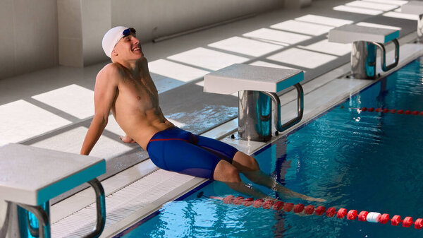 Пловец отдыхает у бассейна с улыбкой после тренировки в солнечном свете. Концепция оздоровления, мотивации, спортивного образа жизни, оздоровления, редакционного содержания и фитнес-рекламы.