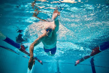 Suyun altında serbest stil hareketinde yüzücü güçlü bir enerjiyle öne bakıyor. Spor kampları kavramı, editörlük kapsamı, motivasyon içeriği, teknik eğitim ve fitness reklamcılığı.