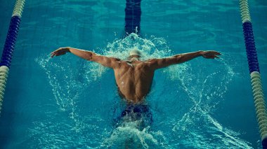 Yarışma havuzunda erkek yüzücünün güçlü kelebek vuruşu. Atletik güç, profesyonel yüzme, spor reklamcılığı, fitness içeriği ve patlayıcı enerjiyle motivasyon kavramı.