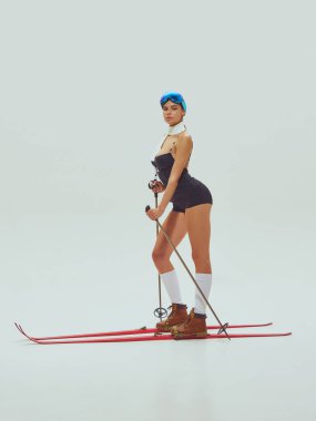 Kırmızı kayak takımları ve beyaz arka planda direklerle siyah kayak kıyafeti giyen çekici bir kadın. Kış modası konsepti, lüks yaşam tarzı makaleleri, cesur reklamlar ve seyahat kampanyaları..