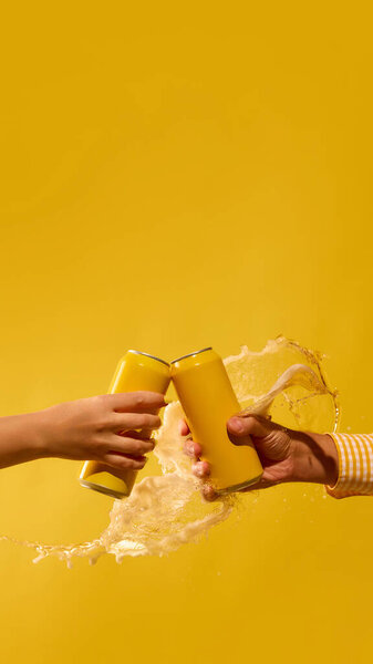 Beer cans clinking with splash on vivid yellow background. Concept of beverage advertising, social media marketing, monochromatic visuals and bold youth lifestyle campaigns. Mockup for text, ad