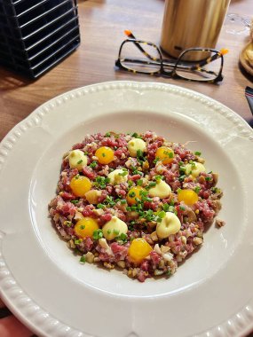 Bir tabak biftekli tartar, çiğ yumurta, mayonez ve soğanla süslenmiş modern bir biftek versiyonu.