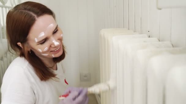 Mulher em uma luva pintando um radiador de aquecimento com um rolo de tinta em casa. Um reparo DIY . — Vídeo de Stock