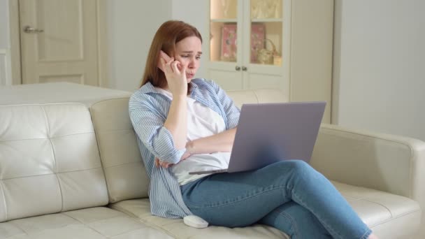 Frau sitzt auf Sofa mit Laptop und telefoniert. teilt Gefühle mit Freund. — Stockvideo