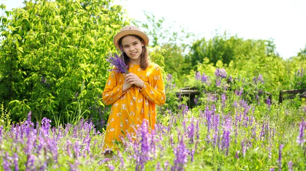Adolescente chica en sombrero recogiendo un ramo de flores silvestres en un prado . — Foto de Stock
