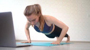 Kız evde dizüstü bilgisayarla spor yapıyor. şınav ve kalas