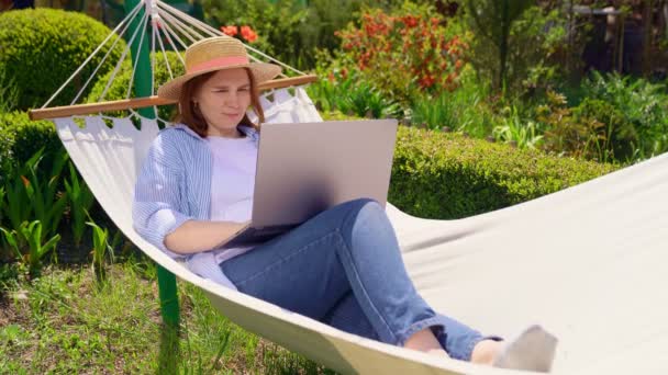 Woman in hat lies in hammock and working on the computer — Stock Video