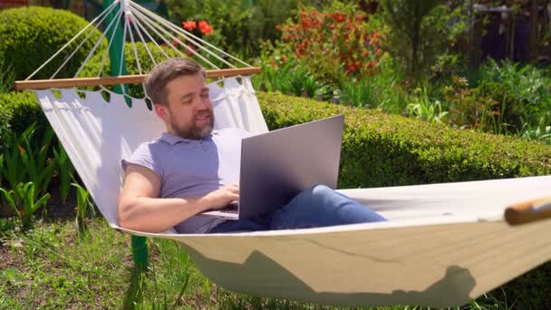 男人躺在吊床上，在电脑上工作，喝果汁. — 图库视频影像