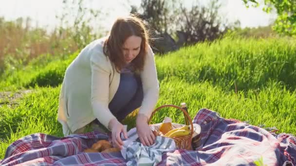Mulher estabelece croissants na toalha para piquenique. cobertor e cesta de alimentos . — Vídeo de Stock