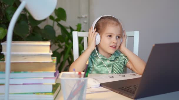 Dziecko dziewczyna w słuchawki słucha lekcji, odległość online nauka w domu — Wideo stockowe