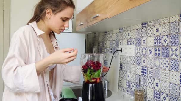 Piękna dziewczyna przygotowuje smoothie w blenderze w jego kuchni. — Wideo stockowe