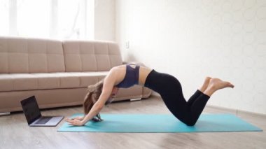 Güzel sporcu kız sporla meşgul. Evde dizüstü bilgisayarda fitness.