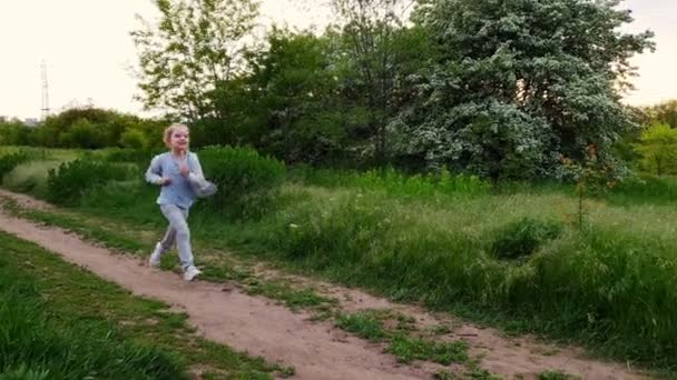 Een klein meisje loopt op een voetpad in het veld. actieve rust op de natuur. — Stockvideo