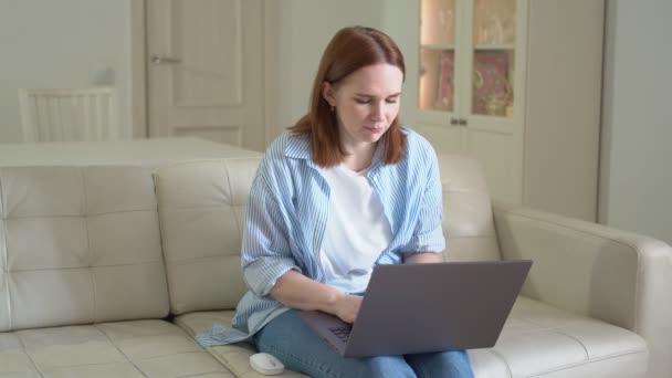 Mujer usando el ordenador portátil, escribiendo texto, sentado en el sofá. enfermo y tosiendo en el codo — Vídeos de Stock