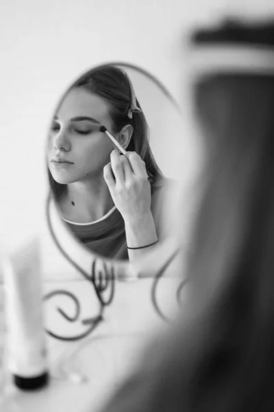 Bianco-nero. bella ragazza facendo make-up e si guarda allo specchio . — Foto Stock