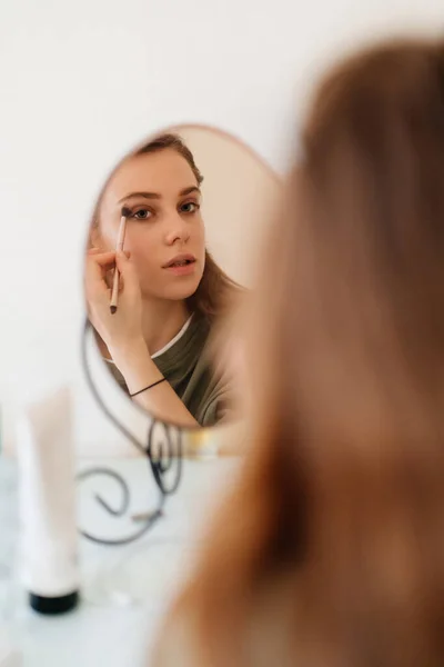 beautiful girl doing make-up and looks in the mirror.