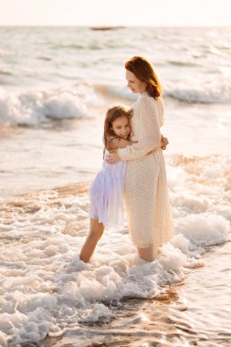 Eğlenceli anne ve çocuk kumsalda rüzgarlı havada dalgalarla yürüyor. Mutlu aile