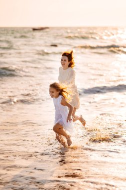 Eğlenceli anne ve çocuk kumsalda rüzgarlı havada dalgalarla yürüyor. Mutlu aile