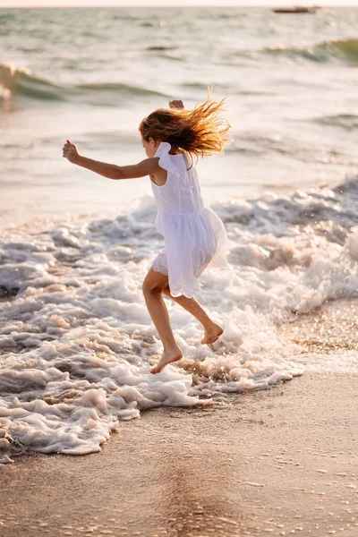 Девушка в белом платье прыгает через волны на пляже. прогулка по морю. отпуск . — стоковое фото
