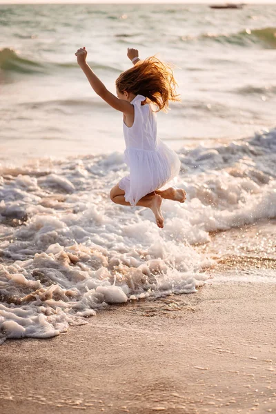 Девушка в белом платье прыгает через волны на пляже. прогулка по морю. отпуск . — стоковое фото