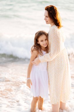 Eğlenceli anne ve çocuk kumsalda rüzgarlı havada dalgalarla yürüyor. Mutlu aile