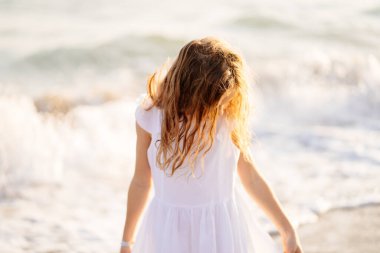 Kız büyük dalgalar ve güçlü rüzgarlarla deniz kıyısında yürüyor ve eğleniyor..